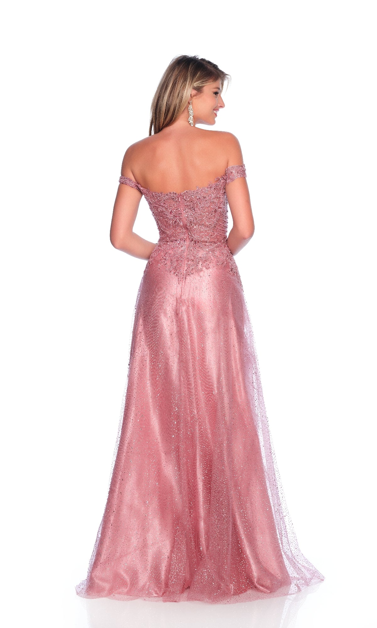 A woman stands facing away in the Mauve Pink Prom Dress: Dave & Johnny 12084, featuring an off-the-shoulder bodice, glitter tulle skirt, and intricate beading. The floor-length gown flares elegantly against a white backdrop.